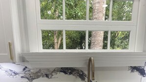 A kitchen with a marble countertop, a stainless steel sink, and white cabinets with gold handles.