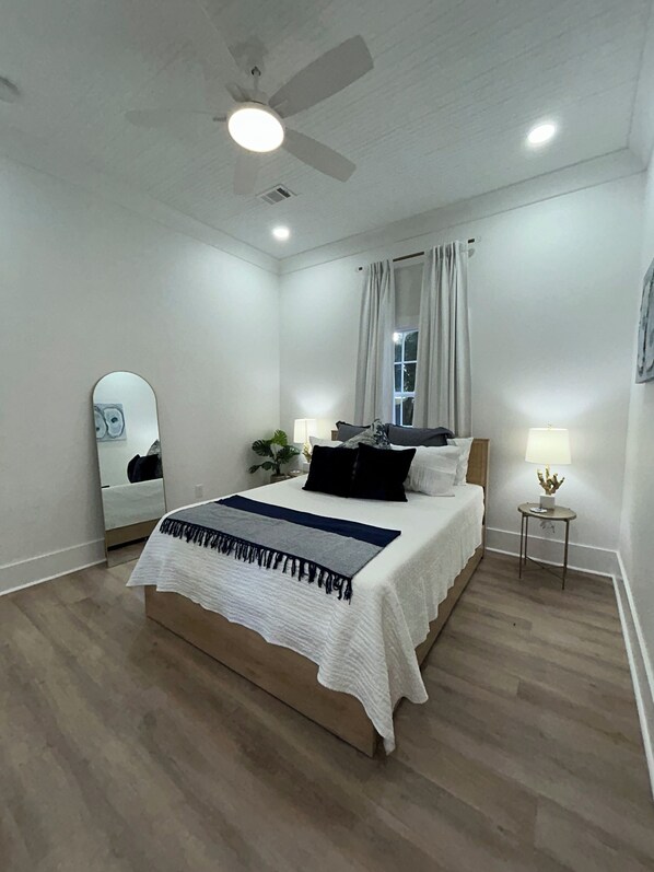 A bedroom with a bed, a ceiling fan, a mirror, a nightstand, and a lamp.