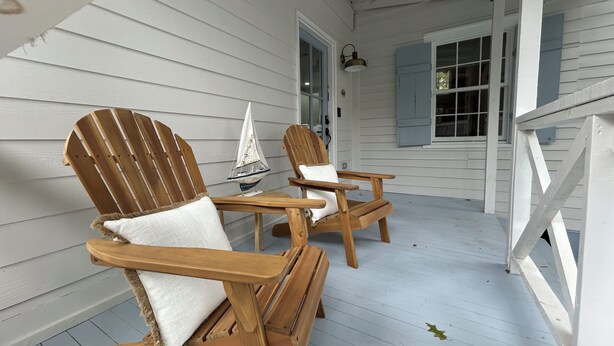 A porch with two wooden Adirondack chairs, a small table, and a sailboat model.