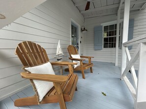 A porch with two wooden Adirondack chairs, a small table, and a sailboat model.