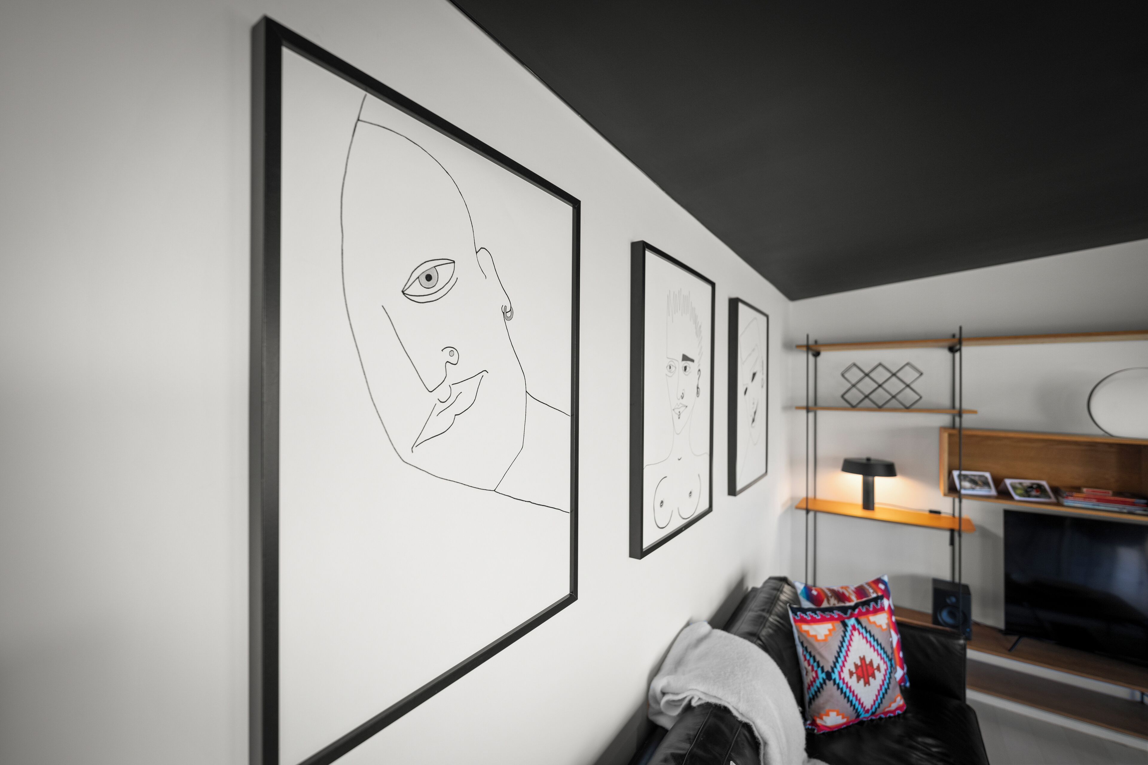 A modern living room with a black leather sofa, a colorful throw pillow, and a large framed artwork on the wall.