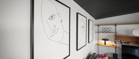 A modern living room with a black leather sofa, a colorful throw pillow, and a large framed artwork on the wall.