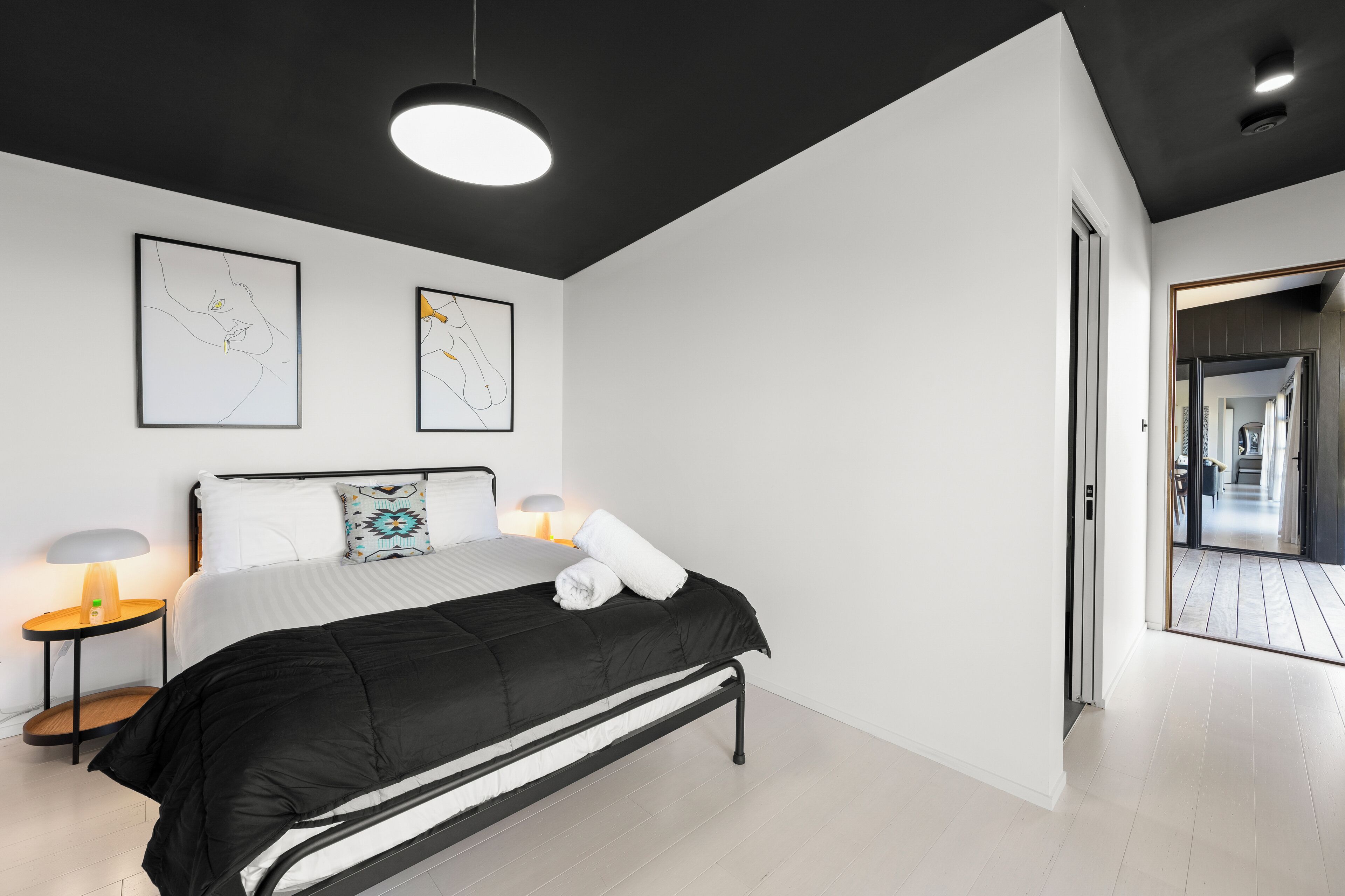 Une chambre à coucher moderne avec un lit noir, des murs blancs et deux œuvres d’art encadrées.