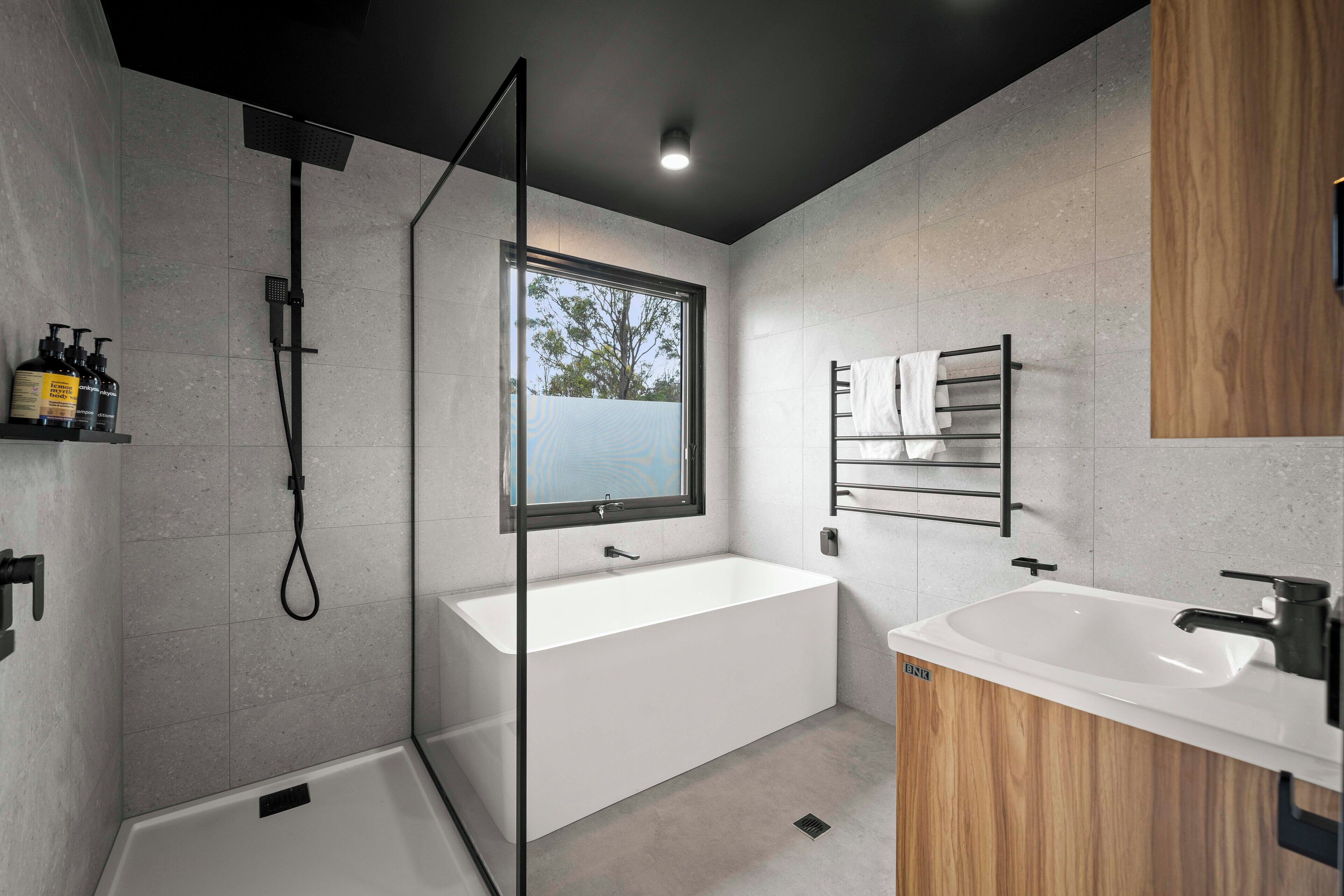 Un baño moderno con ducha de vidrio, una bañera independiente y un tocador con lavabo.