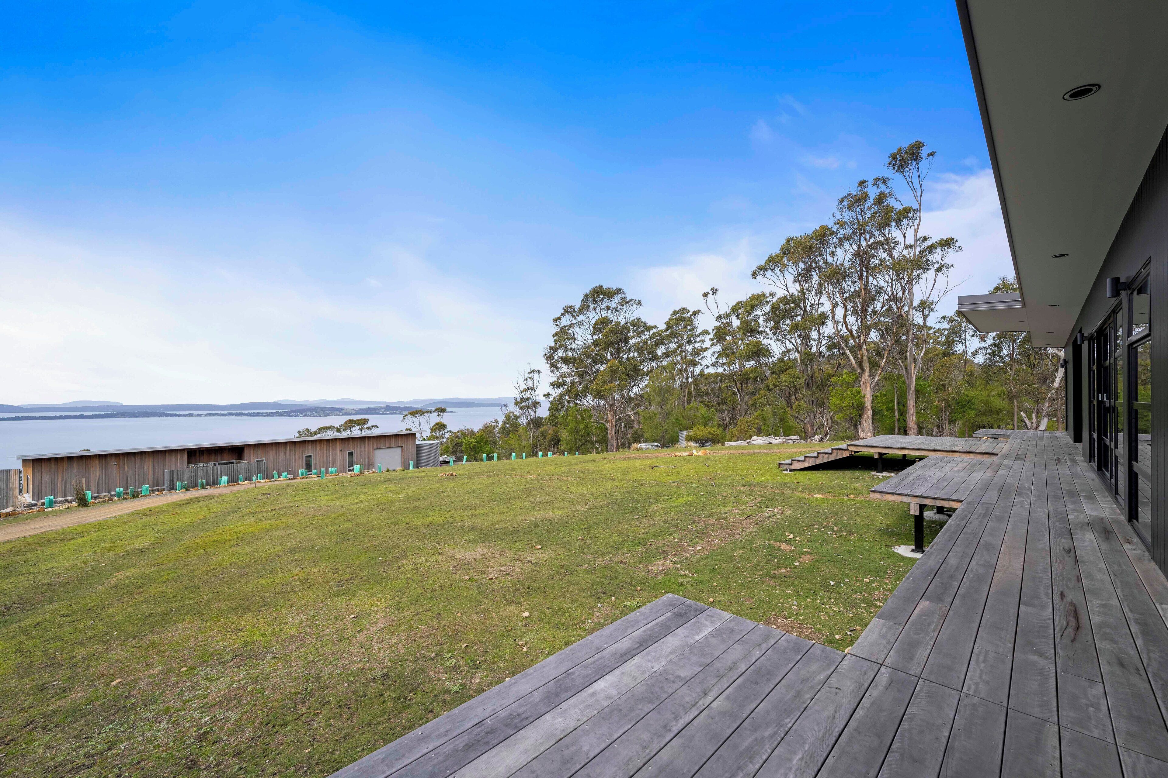 Un bâtiment moderne doté d’une terrasse en bois qui donne sur une zone verdoyante et un plan d’eau.