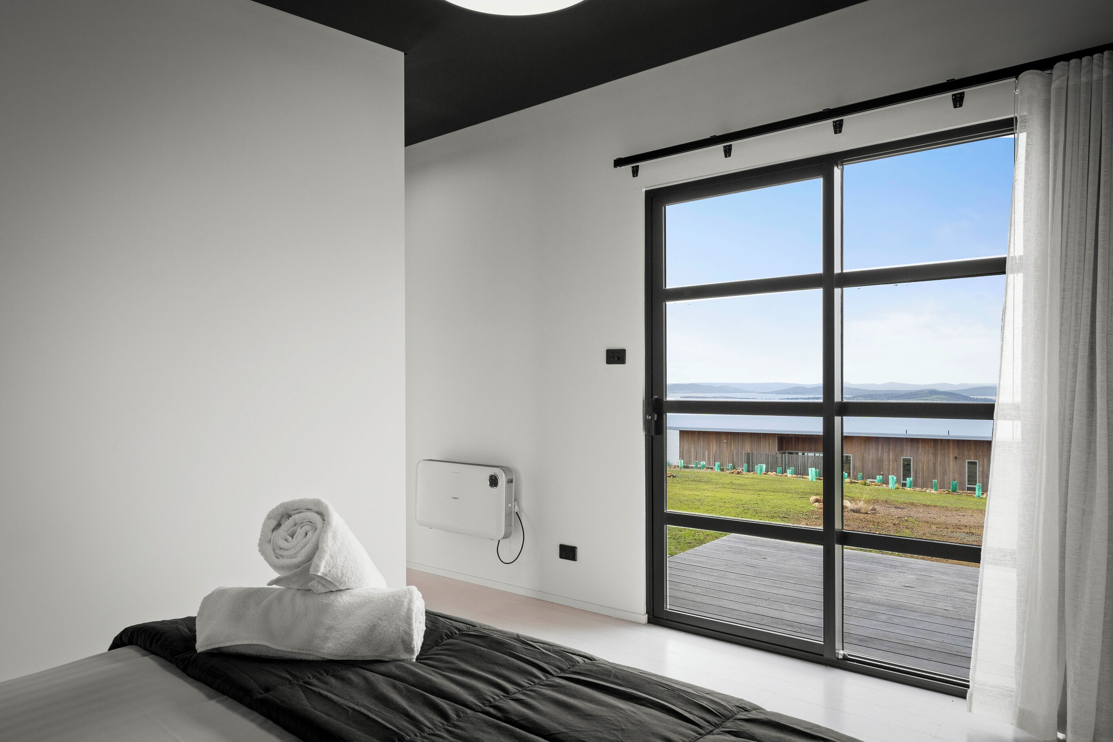 Habitación de hotel moderna con un amplio ventanal corredero a un balcón, una cama bien hecha y un teléfono montado en la pared.