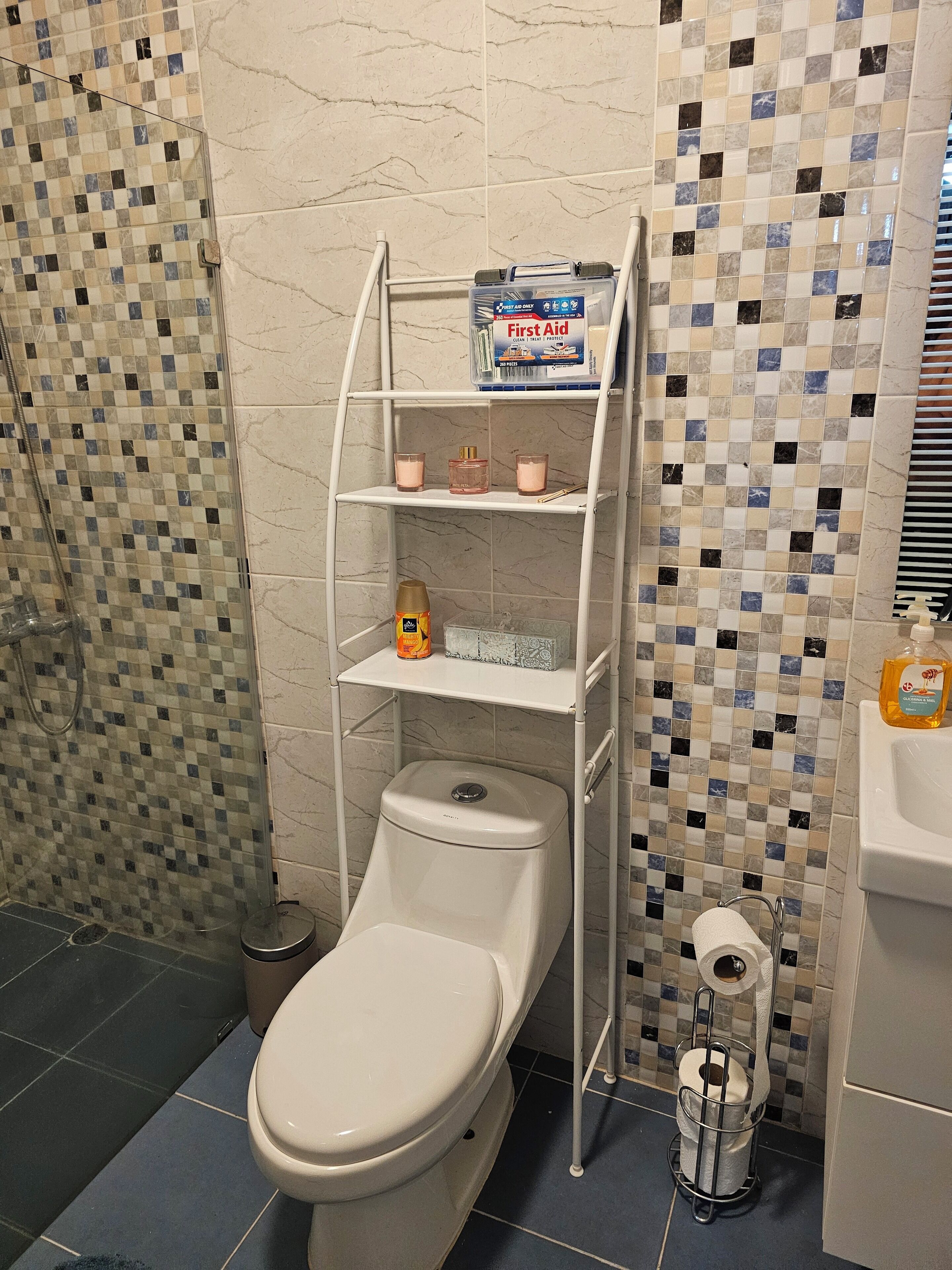 Une salle de bain comprenant des toilettes, une étagère avec des articles de toilette et un espace douche.