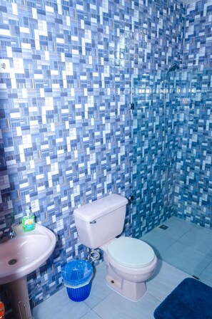 Een badkamer met een betegelde mozaïekwand, toilet, wastafel en douche.