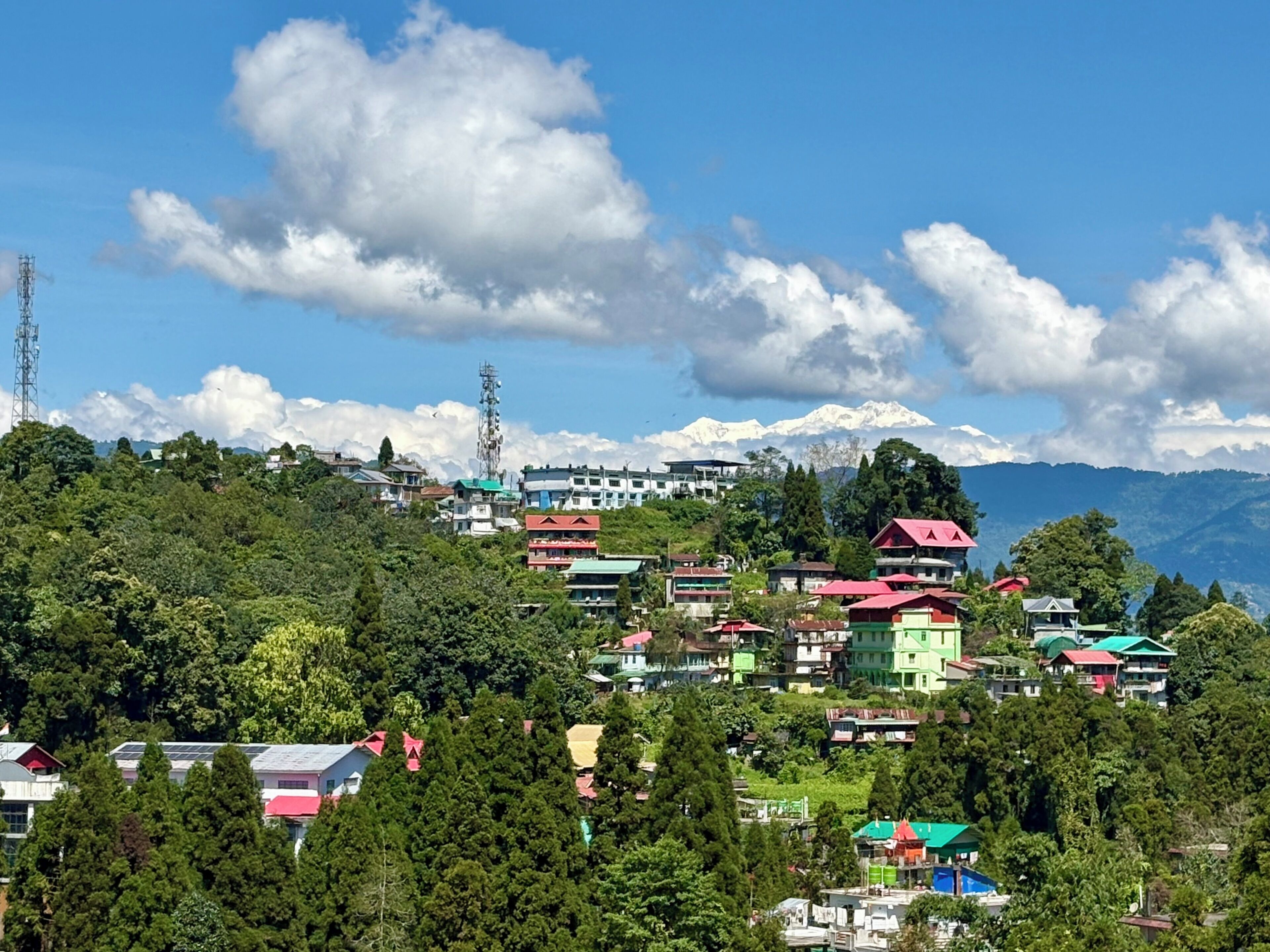 Un village perché sur une colline, avec des maisons aux couleurs vives, une antenne de communication imposante et une chaîne de montagnes en arrière-plan.