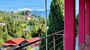 A balcony with a metal railing overlooking a mountainous landscape with buildings and greenery. - Golden Sunview Homesay (Kurseong)