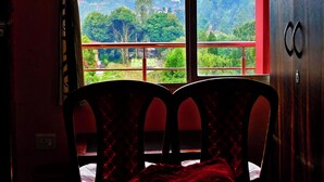 A room with a bed, a window with a view of greenery and hills, and a wardrobe. - Golden Sunview Homesay (Kurseong)
