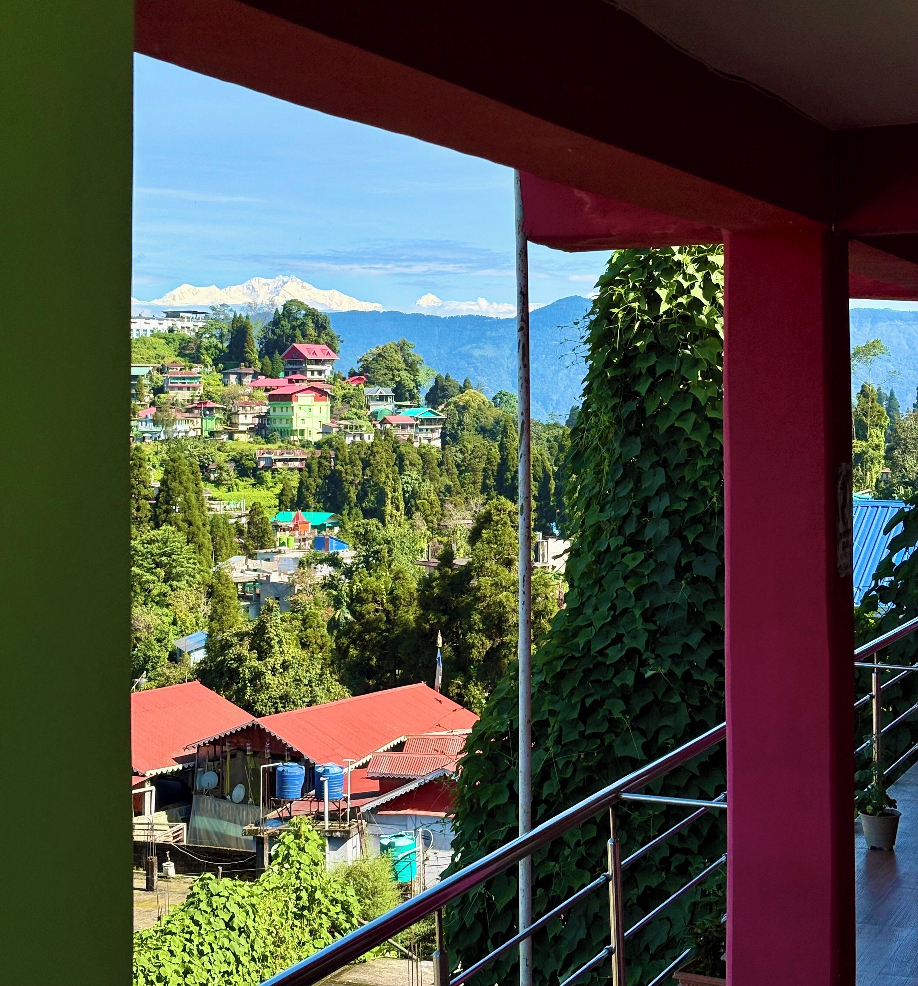 A view from a balcony overlooking a mountainous area with buildings and greenery.