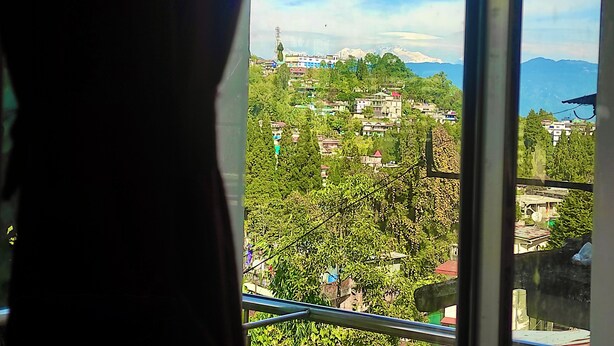 A view from a window overlooking a mountainous area with buildings and greenery. - Golden Sunview Homesay (Kurseong)