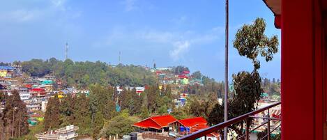 A view from a balcony overlooking a hillside town with buildings and greenery.