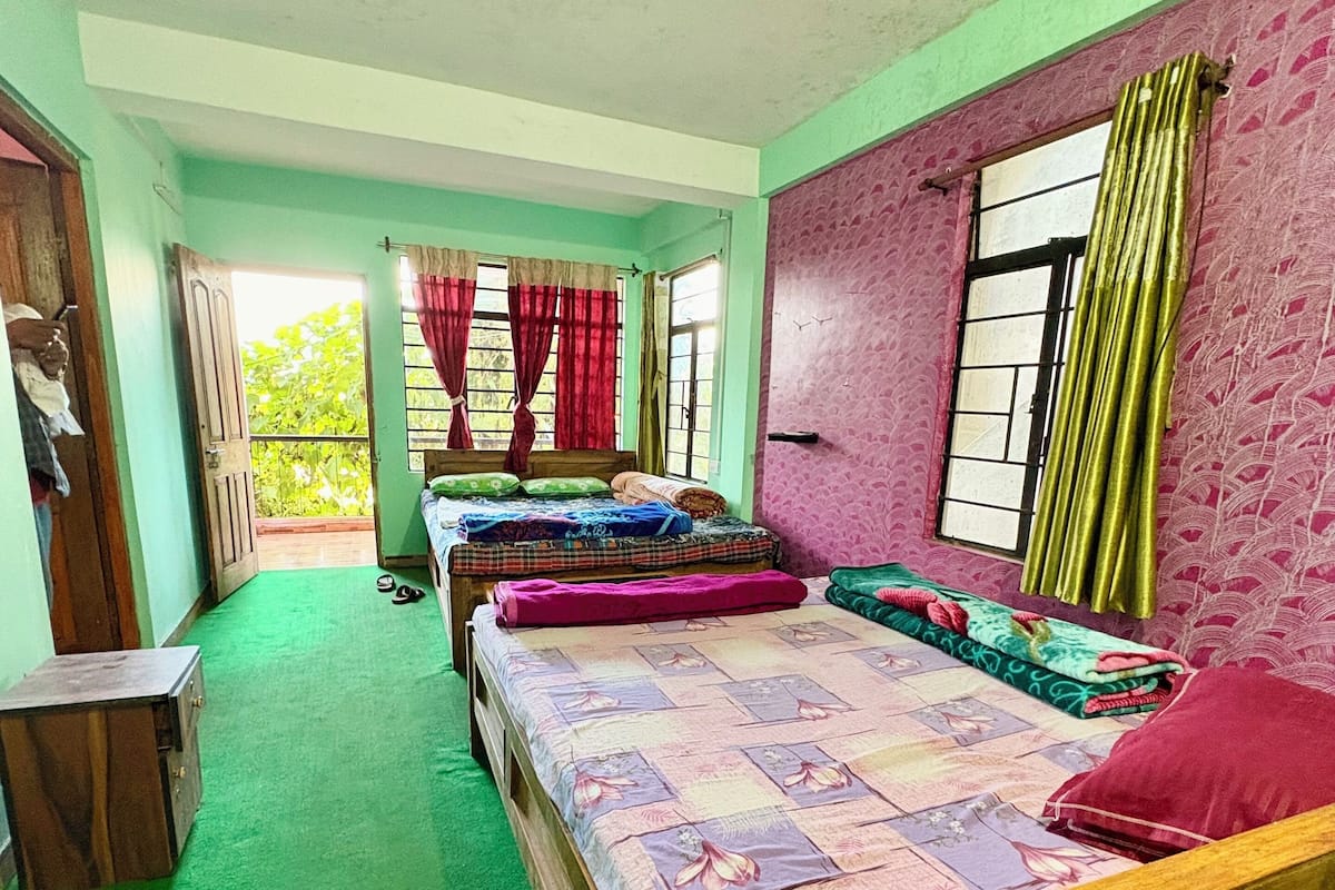 A room with three wooden beds, green carpet, and a view of greenery outside.