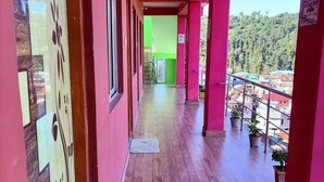 A corridor with wooden flooring, pink walls, and a view of a green area and buildings in the distance. - Golden Sunview Homesay (Kurseong)