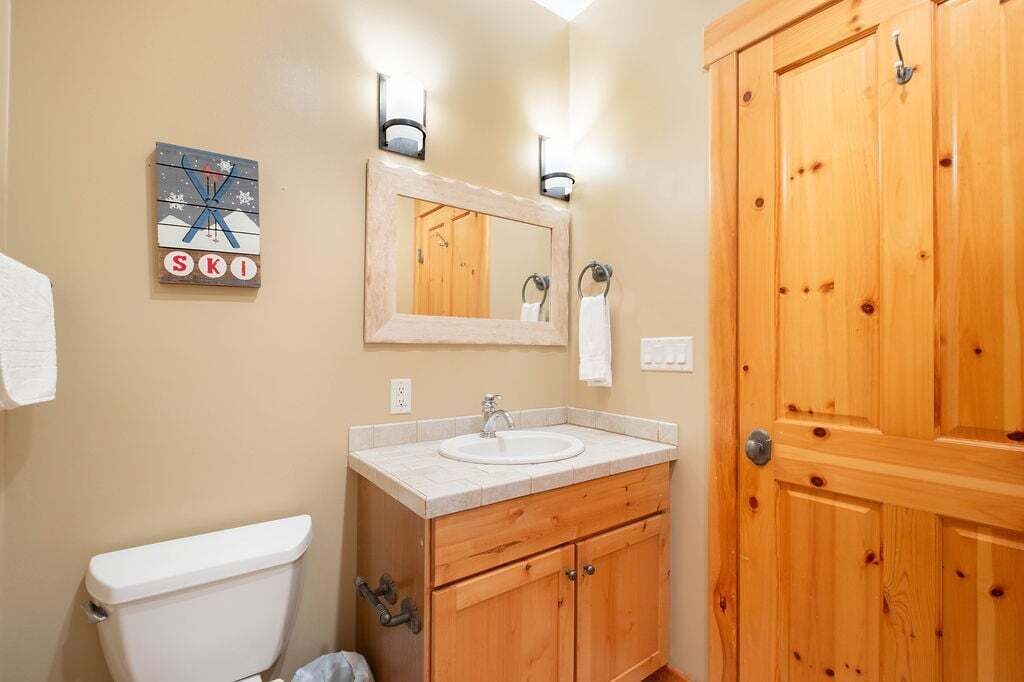 A bathroom with a wooden vanity, a toilet, a mirror, and a wooden door.