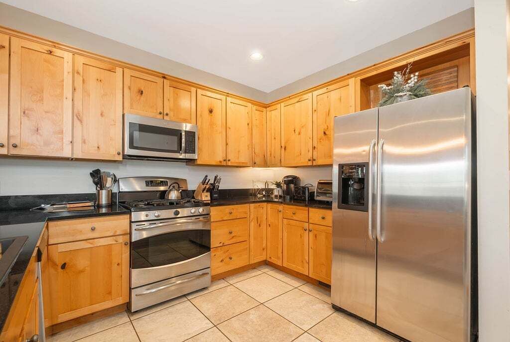 A kitchen with wooden cabinets, stainless steel appliances, and a tiled floor.