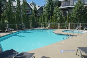 Ein rechteckiger Swimmingpool mit einer gefliesten Kante, umgeben von einer Betonplattform. Liegestühle und ein kleiner Tisch am Pool.