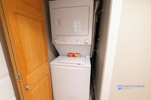 Ein kleiner Waschraum mit Waschmaschine und Trockner, einer Holztür sowie dem sichtbaren Logo von Whistler Superior Properties.