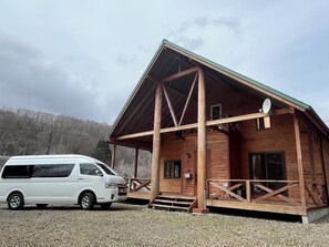 A wooden cabin with a sloped roof, a satellite dish, and a white van parked in front. - A log house with a 100% natural hot spring. (Usu Gun Sobetsu Cho)