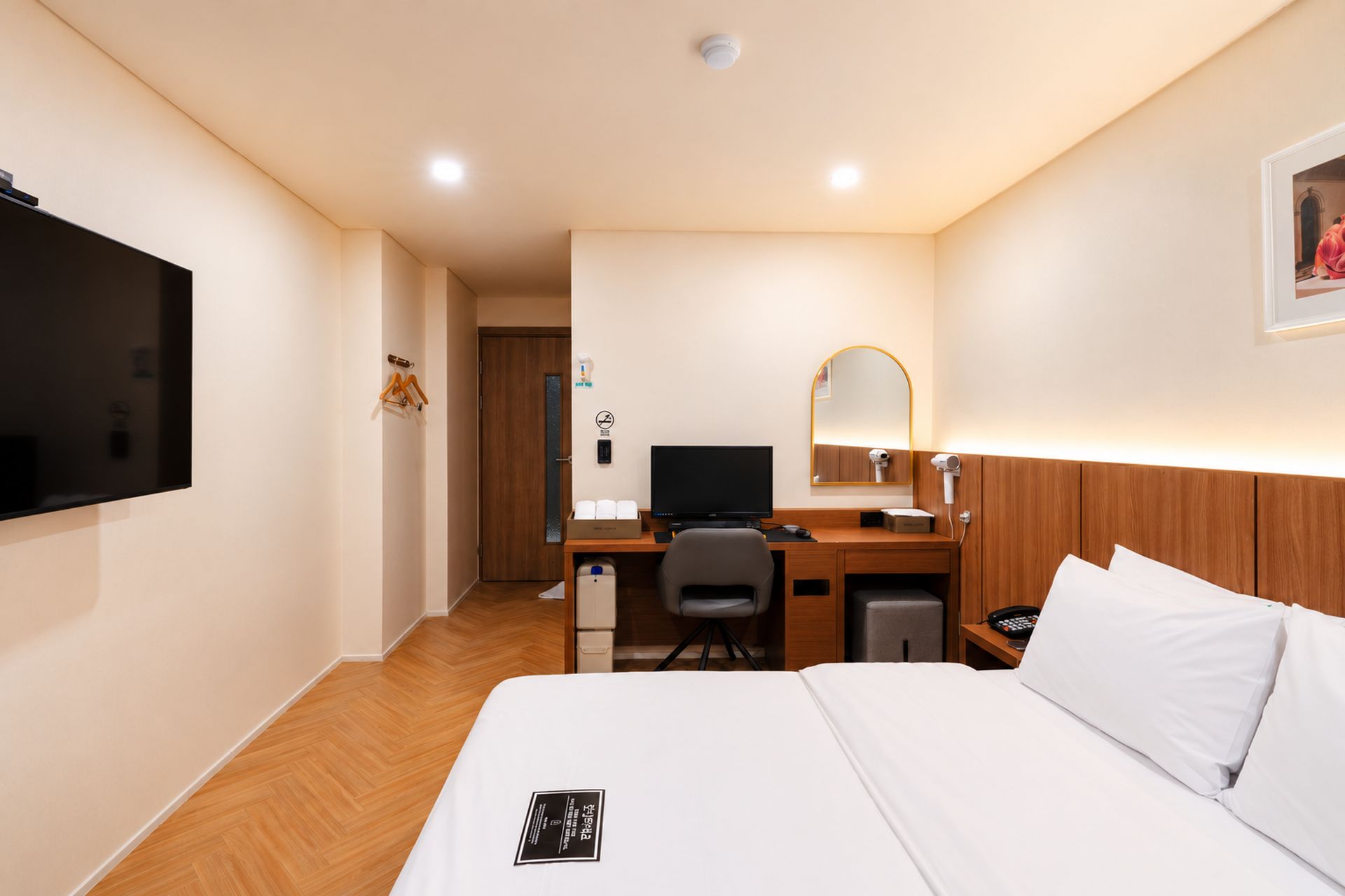 Ein Hotelzimmer mit einem Bett, einem Schreibtisch mit Computer, einem Stuhl, einer Schreibtischlampe und einem Fernseher.