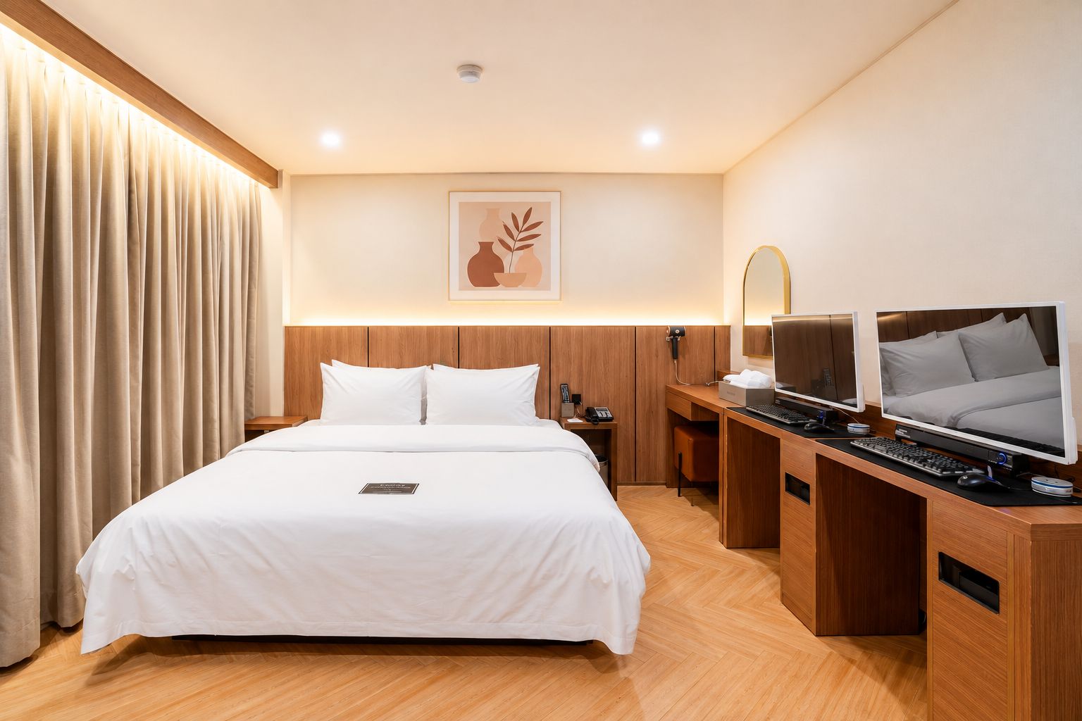 Habitación de hotel con una cama grande, un escritorio con dos monitores, un teléfono y una lámpara de pared.