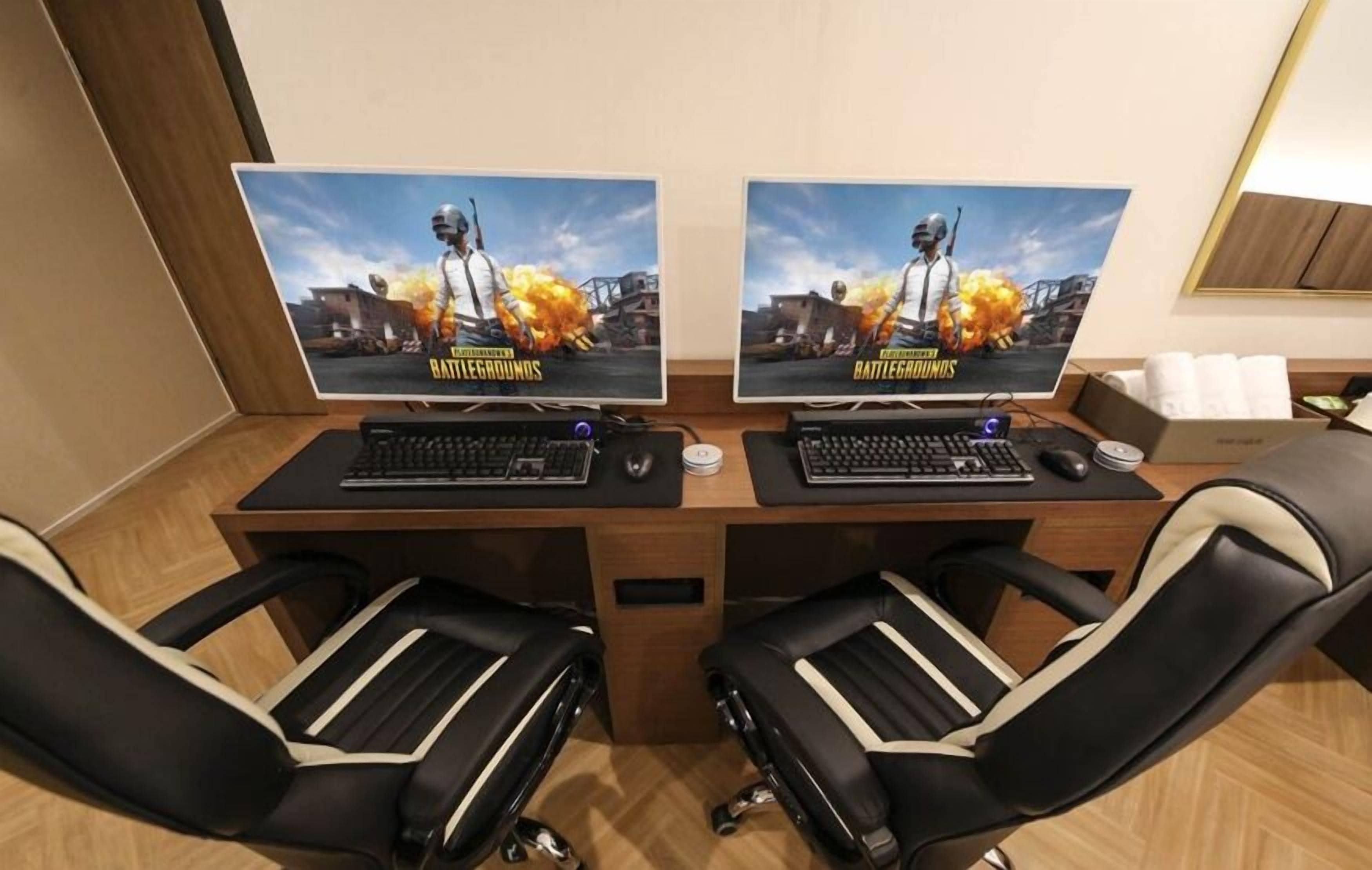 Una habitación con dos estaciones de juego, carteles de 'Battlegrounds', dos sillas de juego negras y un escritorio de madera.