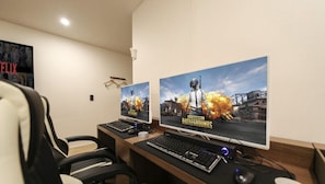 A gaming setup with two monitors displaying 'PUBG' game scenes, a keyboard, mouse, and a chair. - Hotel Laglas Asan (Asan)