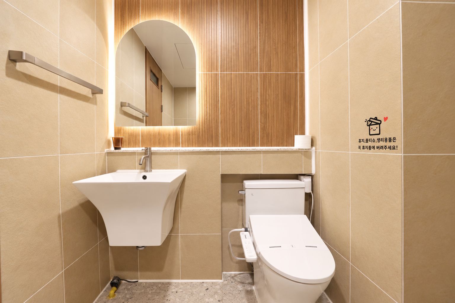 Un bany modern amb un lavabo blanc, un vàter i un armari de tocador de fusta amb un mirall.