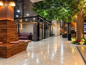 Vestíbulo de hotel con mostrador de recepción, zona de estar y un árbol grande.
