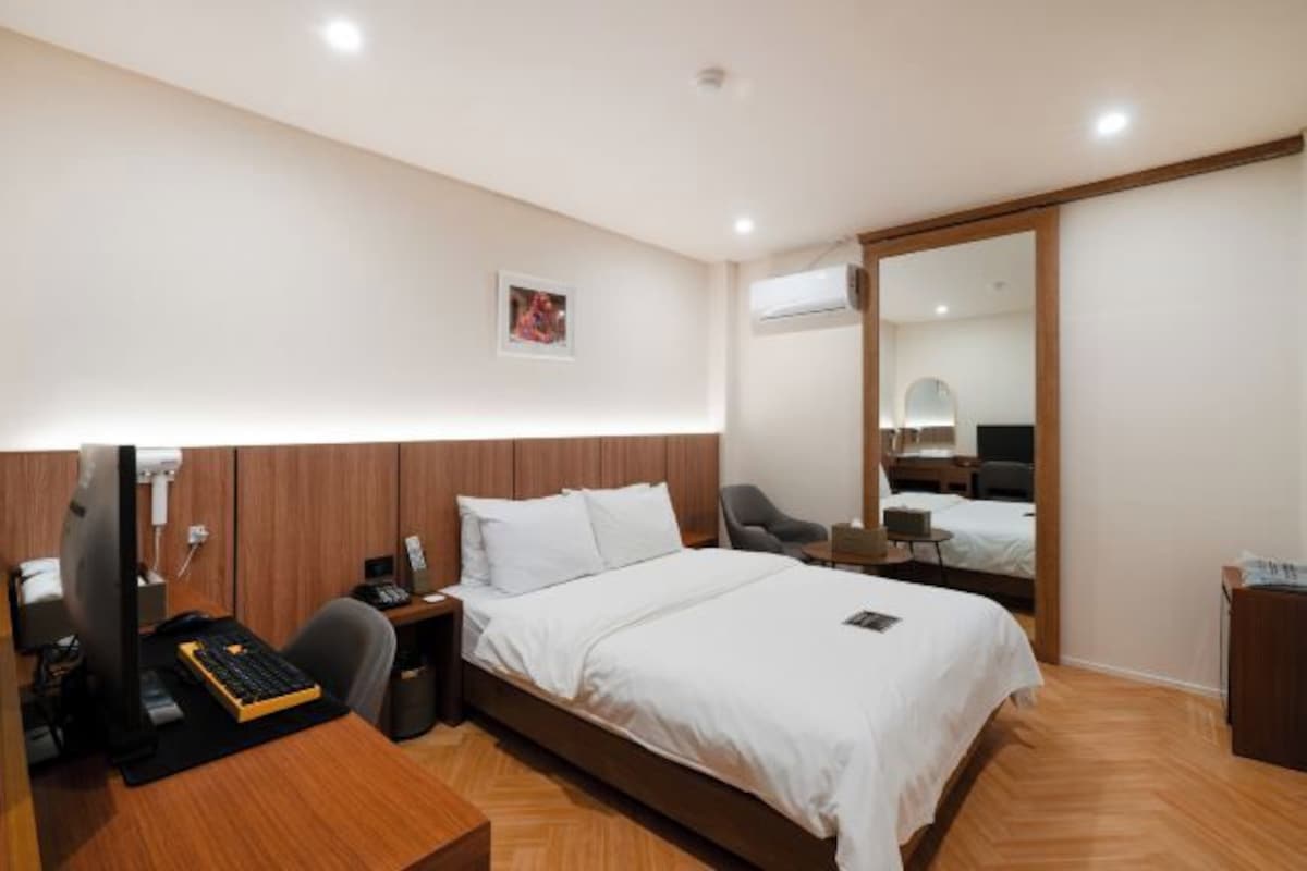 Una habitación de hotel con un escritorio de madera, una cama con ropa de cama blanca, una silla y un espejo.