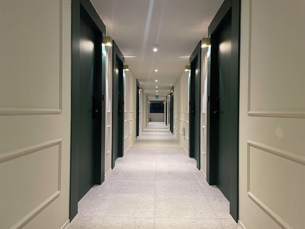 A long, narrow hotel corridor with doors on both sides, recessed lighting, and a tiled floor. - Hotel Laglas Asan (Asan)