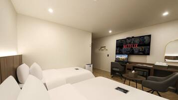Habitación de hotel con dos camas, un escritorio, una silla, un televisor montado en la pared y una mesita.