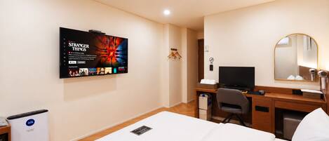 Habitación de hotel con cama, escritorio con computadora, televisor montado en la pared, espejo y calefactor.
