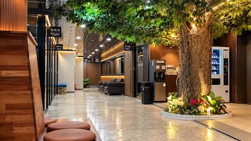Vestíbulo de hotel con mostrador de recepción, zona de estar y un gran árbol artificial.
