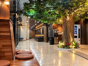 A hotel lobby with a reception desk, seating area, and a large artificial tree. - Hotel Laglas Asan (Asan)