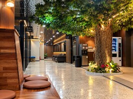 Vestíbulo de hotel con mostrador de recepción, zona de estar y un gran árbol artificial.