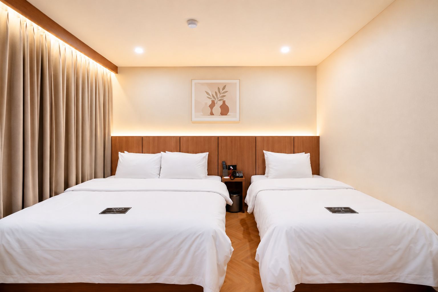 A hotel room with two beds, a wooden headboard, a wall-mounted artwork, and a bedside table with a phone and a trash bin.