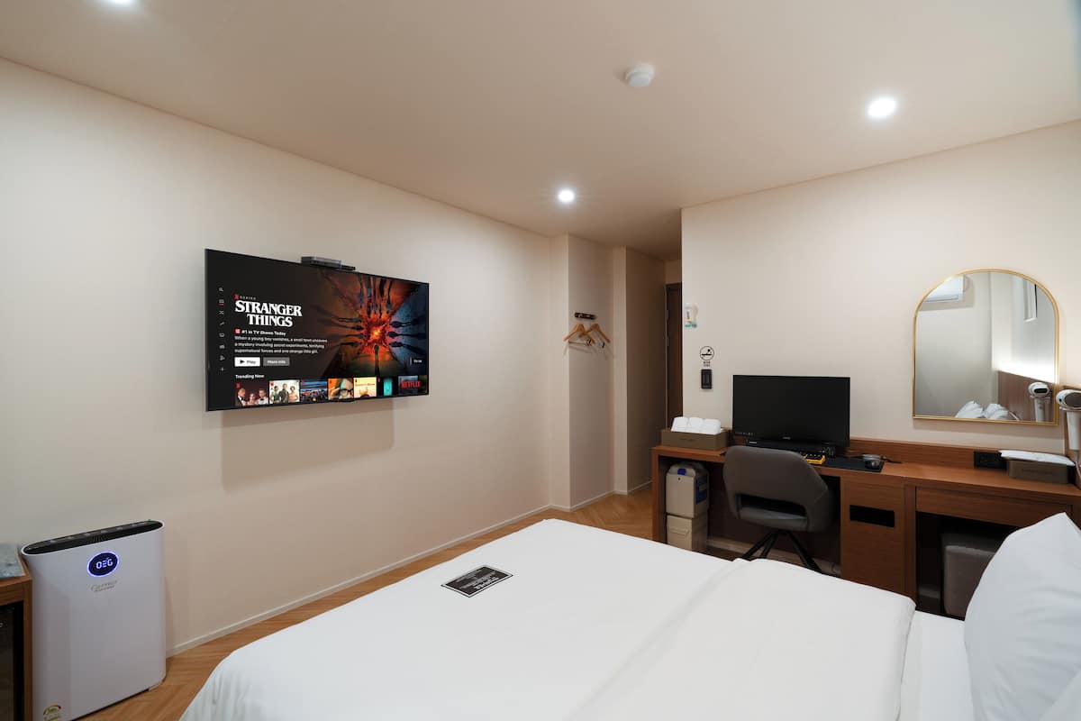 A hotel room with a bed, a desk with a computer, a TV mounted on the wall, and a mirror.