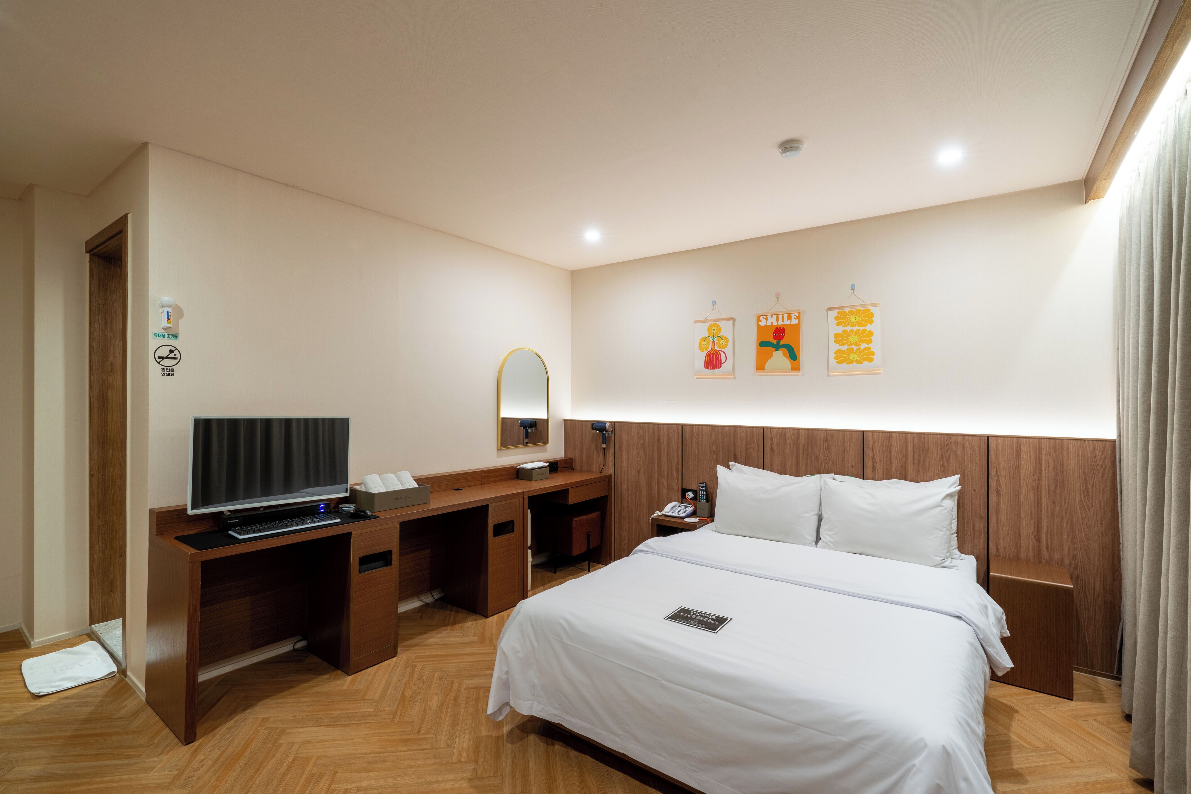 A hotel room with a bed, a desk with a computer, a TV, a mirror, and a nightstand.