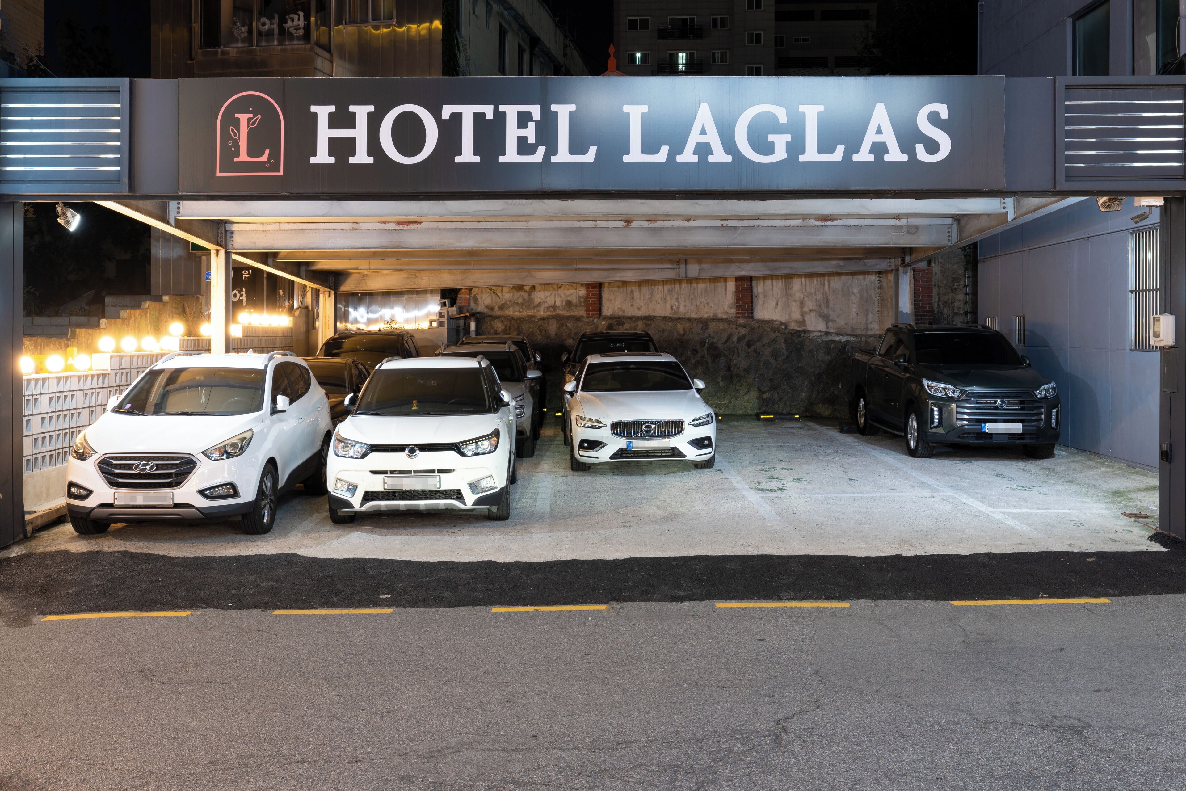 A hotel entrance with a sign reading "HOTEL LAGLAS" and several parked cars.