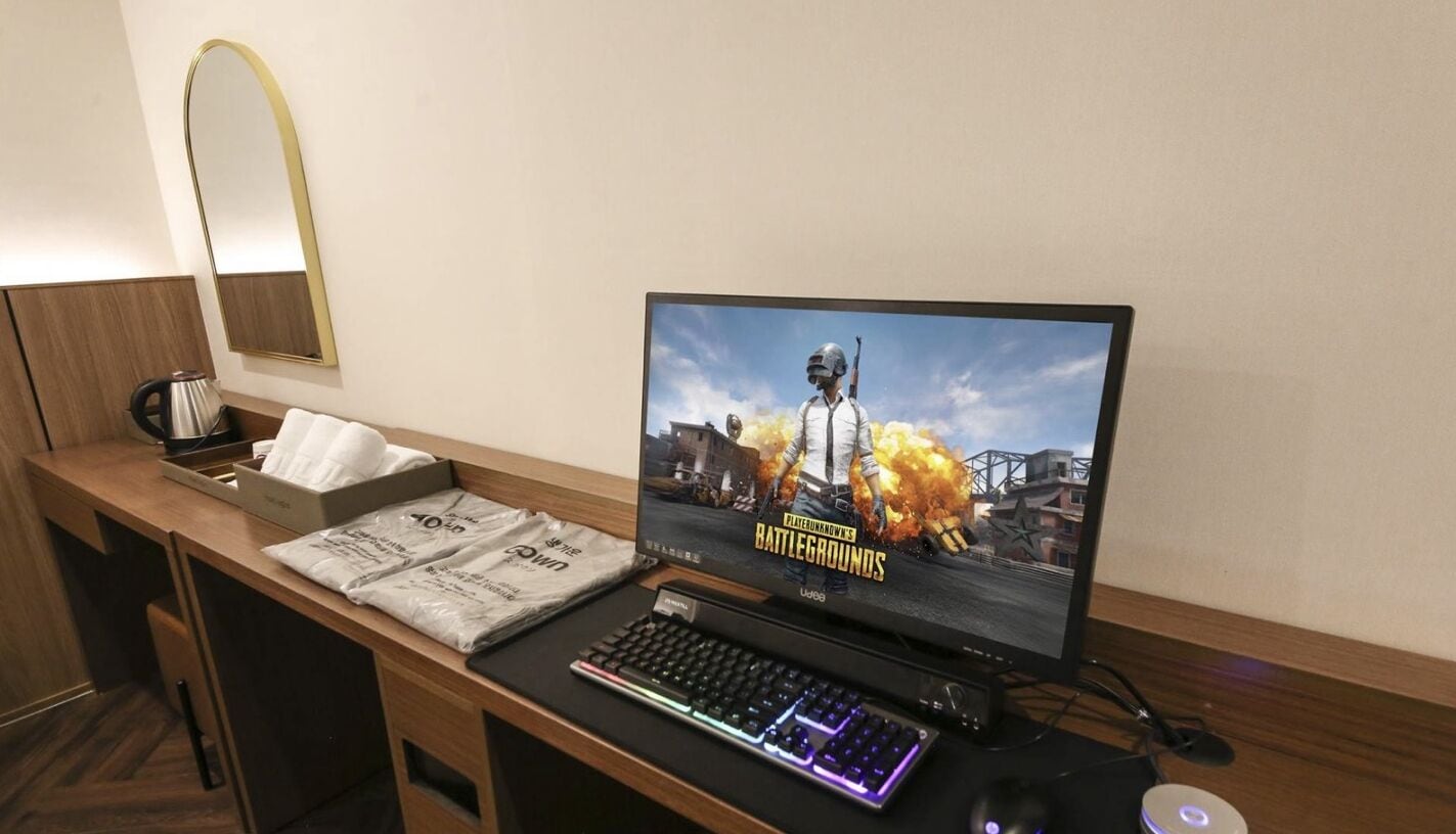 A gaming setup with a monitor displaying a video game, a keyboard, a mouse, and a cup on a wooden desk.