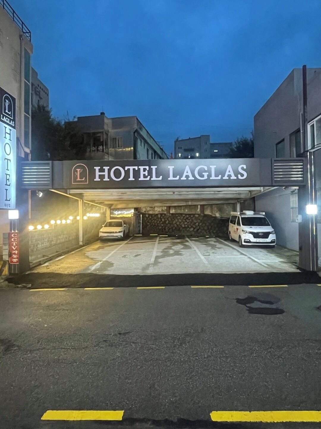 A hotel entrance with a sign reading "HOTEL LAGLAS" and two cars parked inside.