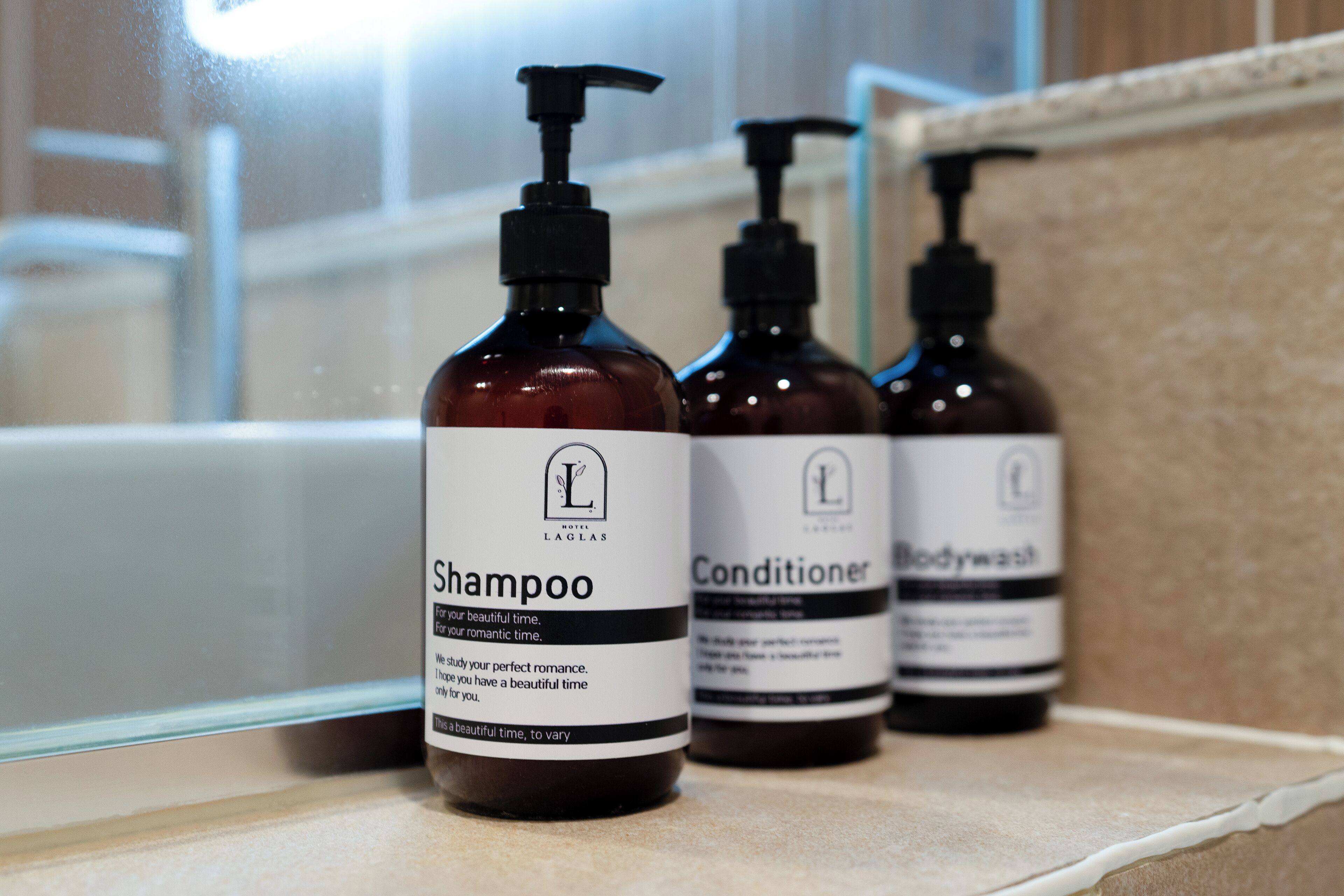 Three bottles of LAGLAS hotel toiletries on a countertop.