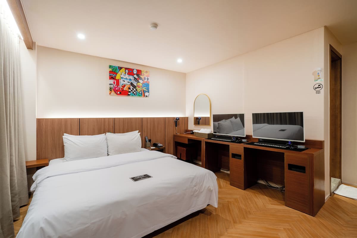 A hotel room with a bed, a desk with a computer, a TV, and a mirror.