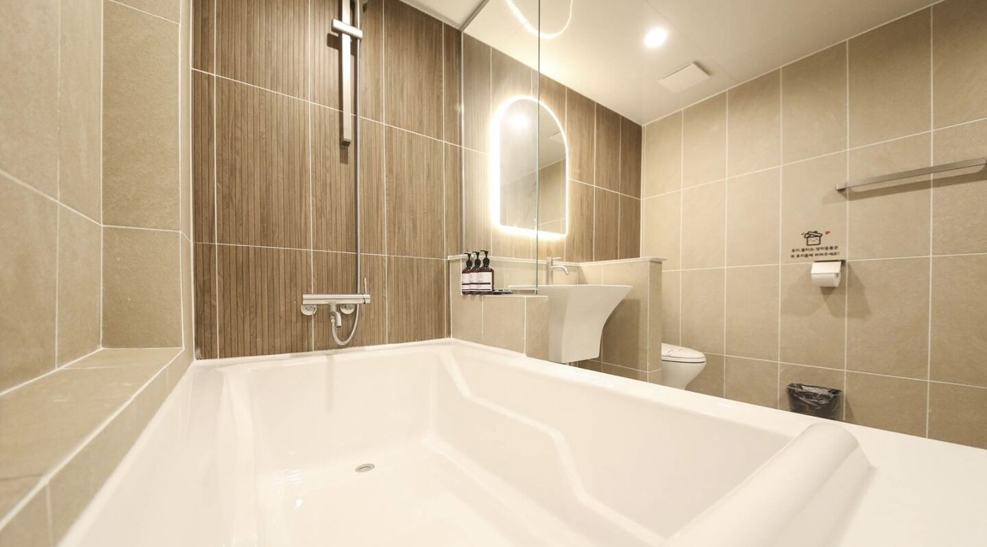 A modern bathroom with a large bathtub, a wooden panel wall, a mirror, and a toilet.
