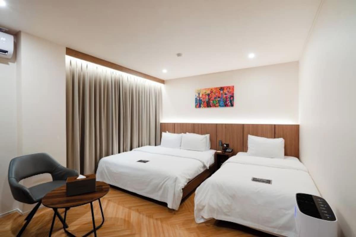 Habitación de hotel con dos camas, un escritorio, una silla, un cuadro en la pared y un equipo de aire acondicionado.