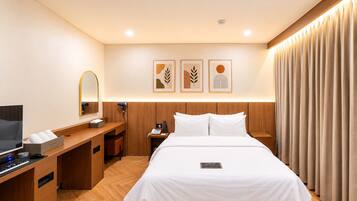 A hotel room with a bed, a desk with a computer, a mirror, and a nightstand.