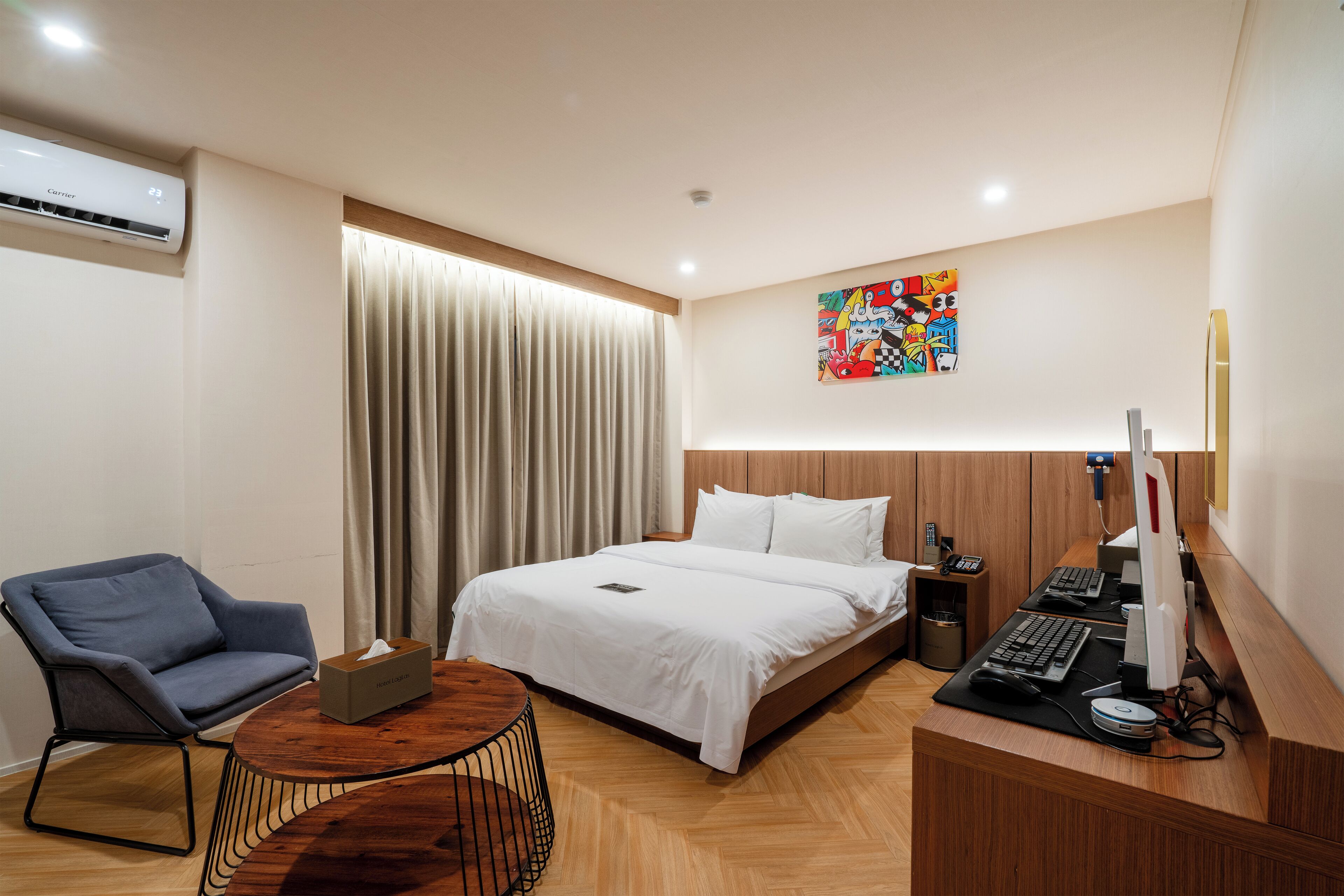 Una habitación de hotel moderna con una cama, un escritorio con una computadora, una silla y una ventana con cortinas.